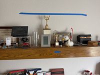 Photo of shelf with various trophies, alarm clock, mugs, and decorative items arranged on a wooden ledge.
