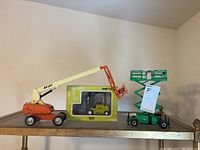 Wide shot showing two JLG lift models and boxed Genex Clark forklift model on a wooden table.