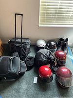 Overview of all items in the lot including helmets, boots, hats, and bags arranged against a wall and window with taped floor.