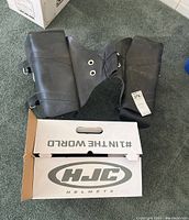 Black leather motorcycle saddle bags laid on carpet next to white HJC helmet shield box.