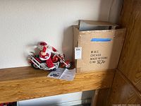 Photo showing Santa Claus figurine on red motorcycle with chrome details next to its original box.