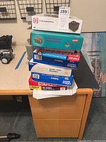 Stack of office supply items including various unopened boxes of hanging folders, manila file folders, and box of CD jewel cases.