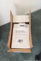 Opened cardboard box containing product manuals and documents for a power booster assembly.