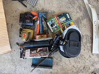 Photo showing a collection of power tools and accessories including a caulk gun, a boxed power meter, a handheld saw, and a black carrying case.