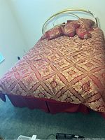 Full view of the made bed showing the brass style metal frame, comforter, and pillows with intricate pattern in red and gold colors.