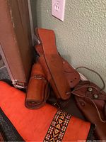 Cluster of orange suede case, brown leather holsters and straps against wall outlet