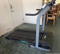 Side view of black and gray treadmill showing treadmill belt and sturdy frame with power cord on carpeted floor near a door.