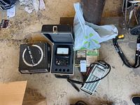 Overview of all items on the floor showing a vintage 12 volt battery tester, Range Doubler Multitester in box, analog multimeter, and small circular tester.