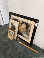4 framed pieces of wall art leaning against wall with rolled poster beside them on carpet
