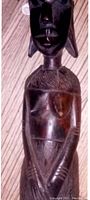 Close-up of the front of the carved ebony female statue showing facial features, textured body carvings, and hands position.