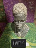 Full view of the African stone statue showing the bust with textured hair and necklace detail, set against patterned background.