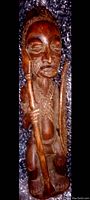 Front view of the African tribal wooden statue carved in light brown wood, showing facial details, staff, and body features.