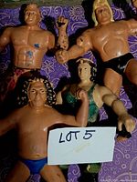 Four 1980s WWF wrestling figurine toys showing signs of wear, with some paint loss and scuffs. Posed on purple patterned fabric background with Lot 5 tag visible.