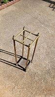 Full view of a vintage brass umbrella holder standing on a concrete surface, showing its full rectangular structure and brass finish.