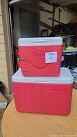 Two Coleman coolers stacked on a wooden table, smaller cooler on top of larger one, both red with white lids