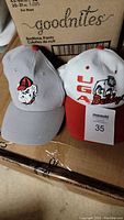 Two Georgia Bulldogs caps placed on boxes, front view showing design details.