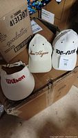 Three vintage golf hats on top of cardboard boxes: Ben Hogan, Top-Flite, Wilson visor.