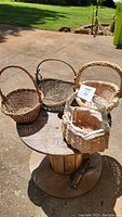 View of four woven baskets on a wooden spool outdoors, showing variety of sizes and colors.