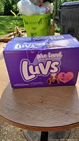 Box of Luvs Pro Level Leak Protection size 5 diapers, 92 count, on a wooden table outdoors.