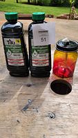 Two bottles of Tiki BiteFighter Torch Fuel and one glass quart jar burner on a wooden surface outdoors.