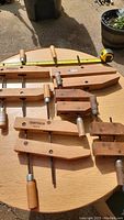 Photo showing five wood clamps of different sizes made of wood with metal screws and wooden handles, laid on a round wooden table with yellow tape measure showing length on top.