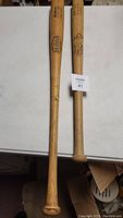 Two wooden baseball bats placed side by side on a white surface, showing full length and handle ends.