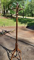 Full view of solid wood hall tree standing outside on a driveway with grass and retaining wall in the background. Shows overall design with rounded hooks and vertical pole.