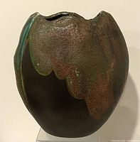 Front view showing textured surface with dark brown glaze and band of iridescent blue-green glaze flowing from top near rim.