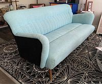 Front-side view of teal blue and black tufted sofa showing angled arm