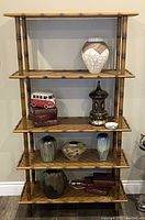 Front view of vintage bamboo and rattan shelf displaying decorative items such as ceramic vases, a model van, books, and a lantern.