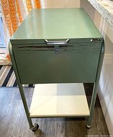 Front view of green metal rolling filing cabinet showing front lock panel with handle and wear marks.