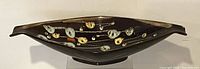 Side angled view showing elongated shape, flared ends, and hand painted abstract floral design on dark brown ceramic.