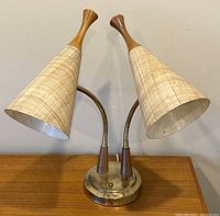 Front view of vintage MCM double gooseneck desk lamp showing dual fiberglass shades with teak finials and curved metal flexible arms from metal base with some tarnish.