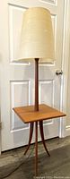 Front view of teak tripod lamp with square tabletop and cream fiberglass shade