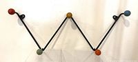 Front view of mid century metal zigzag coat rack with five colorful wooden ball hooks, showing rust and signs of wear.