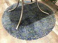 Photo showing the circular vintage shag rug under a metal table base, with a plush thick blue and green shag texture.