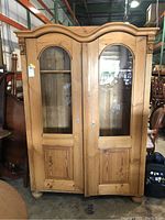 Front view of the wooden armoire showing two glass-paneled doors with wooden panels below and a decorative curved top molding.