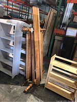 Photo of wooden bed frame parts leaning against shelving units in a storage area. Includes headboard, footboard with spindle/posts, and side boards.