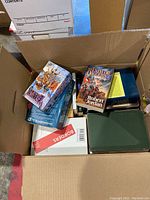 Box with mixed books showing a variety of paperback and hardcover editions, including boxed sets and loose books.