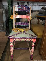 Front view of the colorful hand-painted wooden chair with tassels, showing detailed decoration and patterns on the seat and backrest.