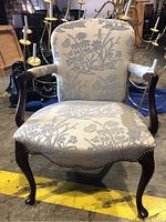Front view of the wood framed chair showing floral upholstery, curved wood arms, and nail head trim.