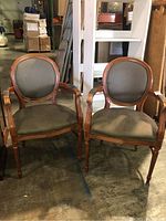 Two matching wood-framed armchairs with striped fabric upholstery and nail head trim, shown side by side in an indoor setting on a concrete floor.