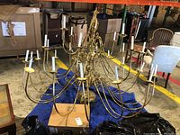 Front view of the large brass chandelier showing multiple arms with candle style light holders and bent/broken rods.