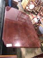 Photo showing the reddish-brown polished wooden tabletop with beveled edges, some scratches and marks visible.