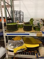 Wide shot of stacked green ceramic plates, mugs, bowls, and a green ceramic pig pitcher with a cardboard pear box on a wooden shelf