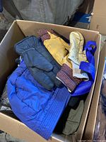 Box with men's gloves in different styles and colors: yellow leather gloves with knit cuffs, black insulated gloves, and knit gloves in another color.