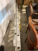 Photo showing the overall ladder length from above, capturing the full ladder laid on the ground next to chairs and other items, highlighting the aluminum silver color and rusted base plates.