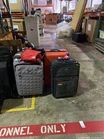 Photo showing all four large wheeled luggage pieces and the small red duffel bag arranged on a warehouse floor.