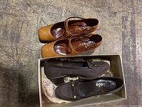 Four pairs of women's shoes including brown loafers with gold buckle, rust-colored lace-up shoes, dark brown slip-ons, and tan Mary Jane style shoes.