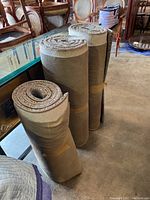 Three rolled grey runner rugs standing upright on a floor with visible bound edges and padded backing.